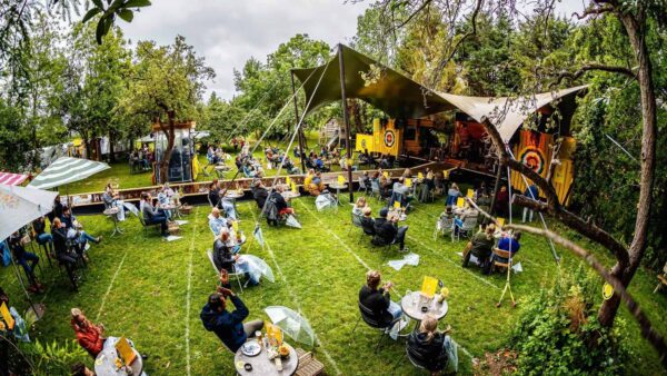 De Brielsche Aap - De Tuin Van 2020 - mensen die op stoelen naar een optreden zitten te kijken in een tuin met eemn stretchtent en podium