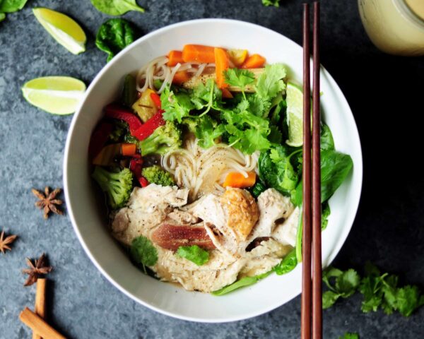 Gerecht met noodles groente en kip in een kom met stokjes erbij - foodtrends