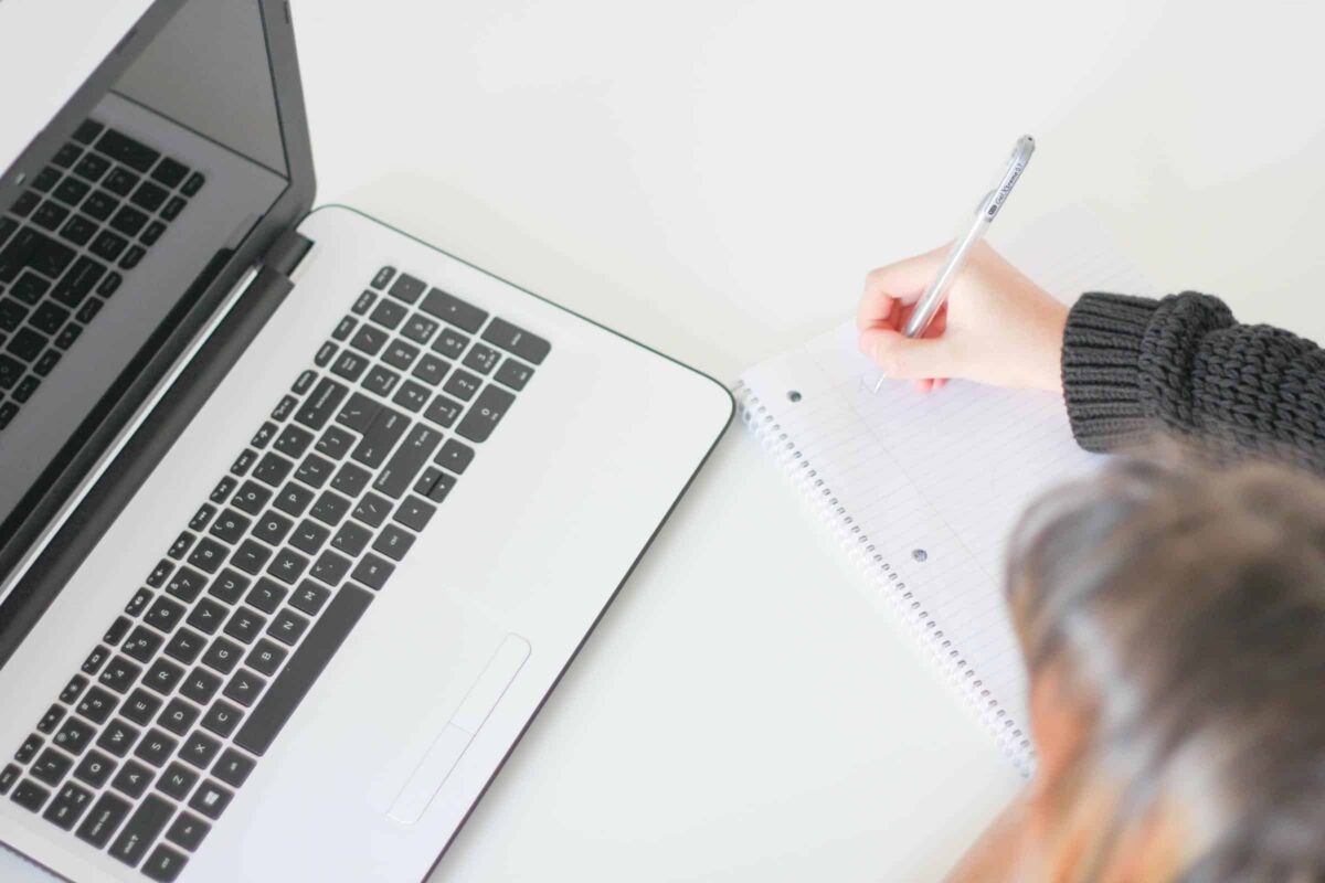 Laptop met schrijfblok en vrouw die iets schrijft