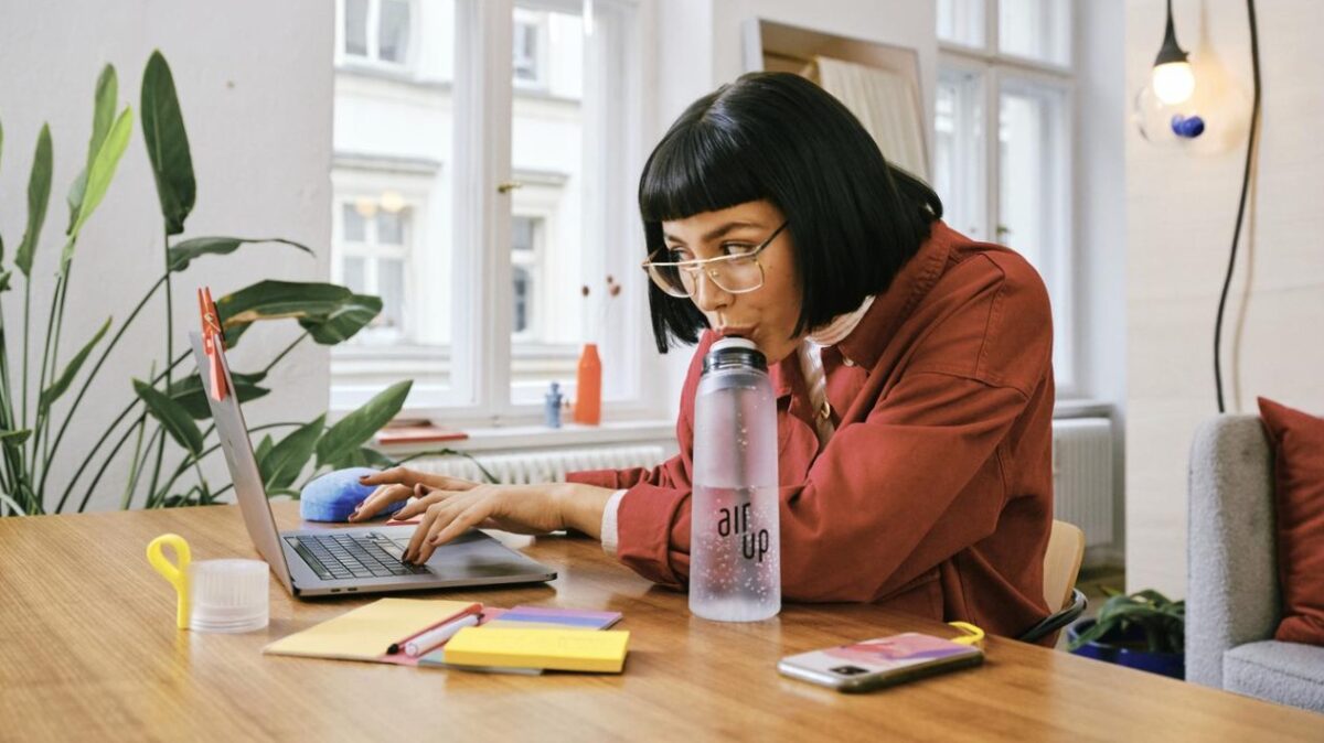 Vrouw achter laptop die aan het drinken is uit een waterfles van air up