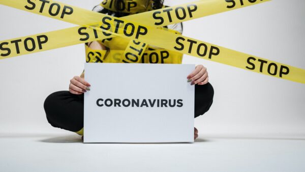 Vrouw ingepakt met geel tape met stop erop en een bord met coronavirus
