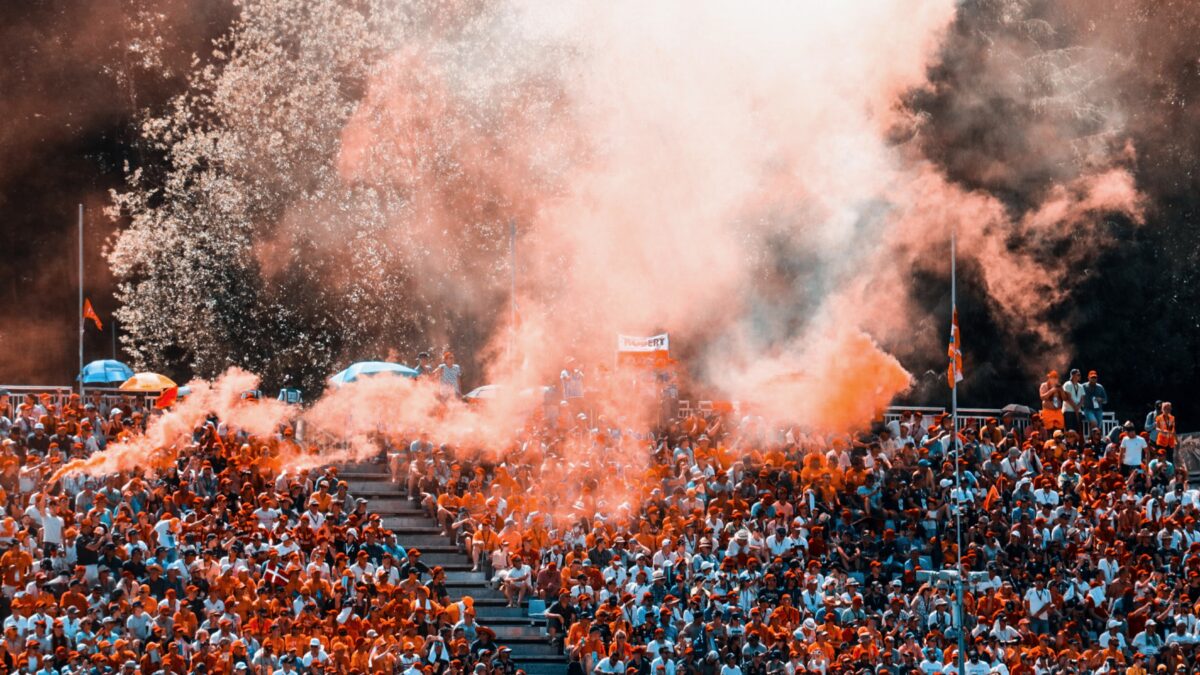 Publiek in oranje kleding en rook in de lucht