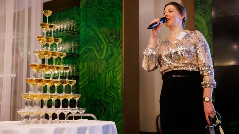 Drink The Moment - vrouw met microfoon bij champagnetoren